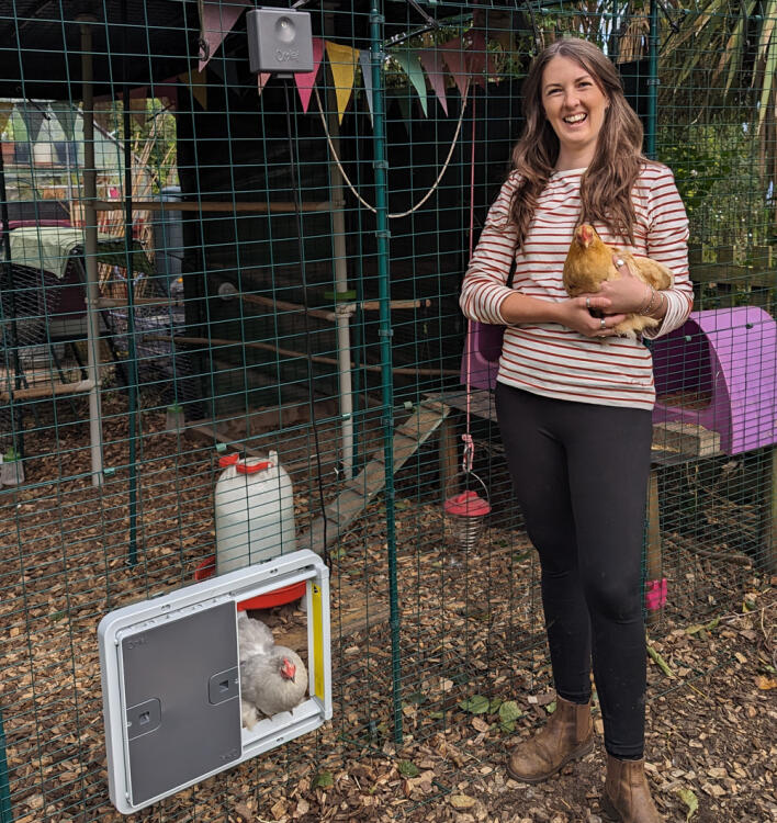 Frau hält ein huhn vor ihrem hühnerstall mit automatischer stalltür